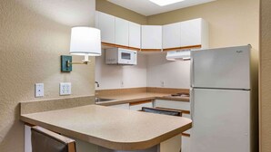 A compact kitchen with white cabinets, a microwave, a refrigerator, and a sink.