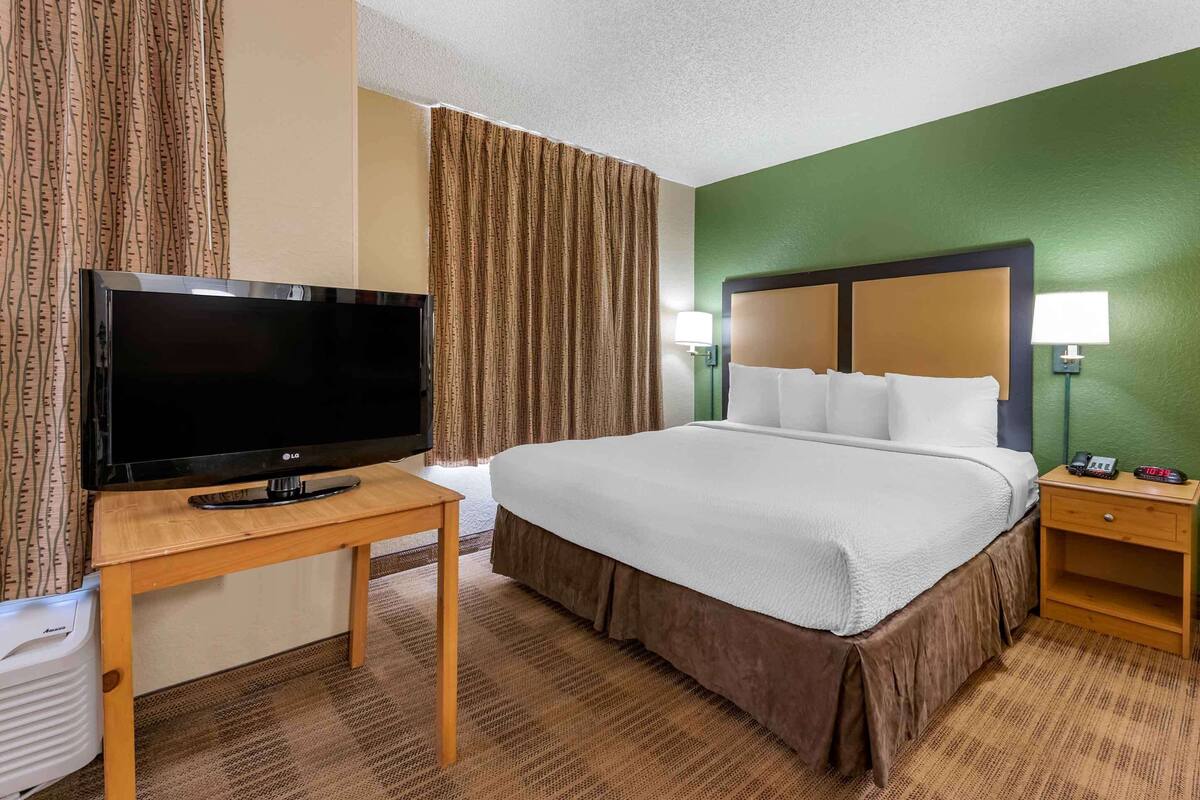 A hotel room with a large bed, a television on a wooden table, a bedside lamp, and a nightstand with a phone.