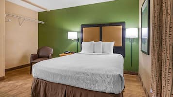 Habitación de hotel con una cama grande, una silla, una mesita de noche con teléfono y una lámpara de pared.