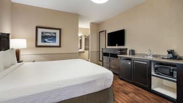 A hotel room with a bed, a desk with a flat-screen TV, a microwave, and a coffee maker.