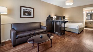 Une chambre d’hôtel moderne avec un canapé en cuir, une table basse en verre, un coin cuisine et un lit.