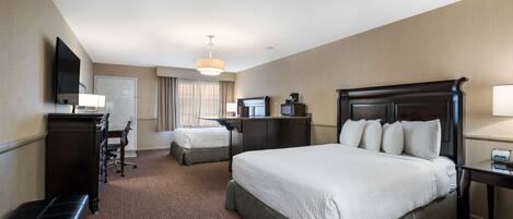 A hotel room with a large bed, a desk with a chair, a television, and a desk lamp.