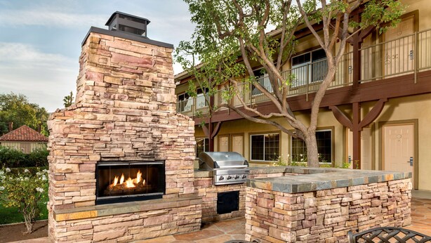 Une cheminée extérieure en pierre avec un barbecue, entourée d’escaliers en pierre et de deux fauteuils en osier.