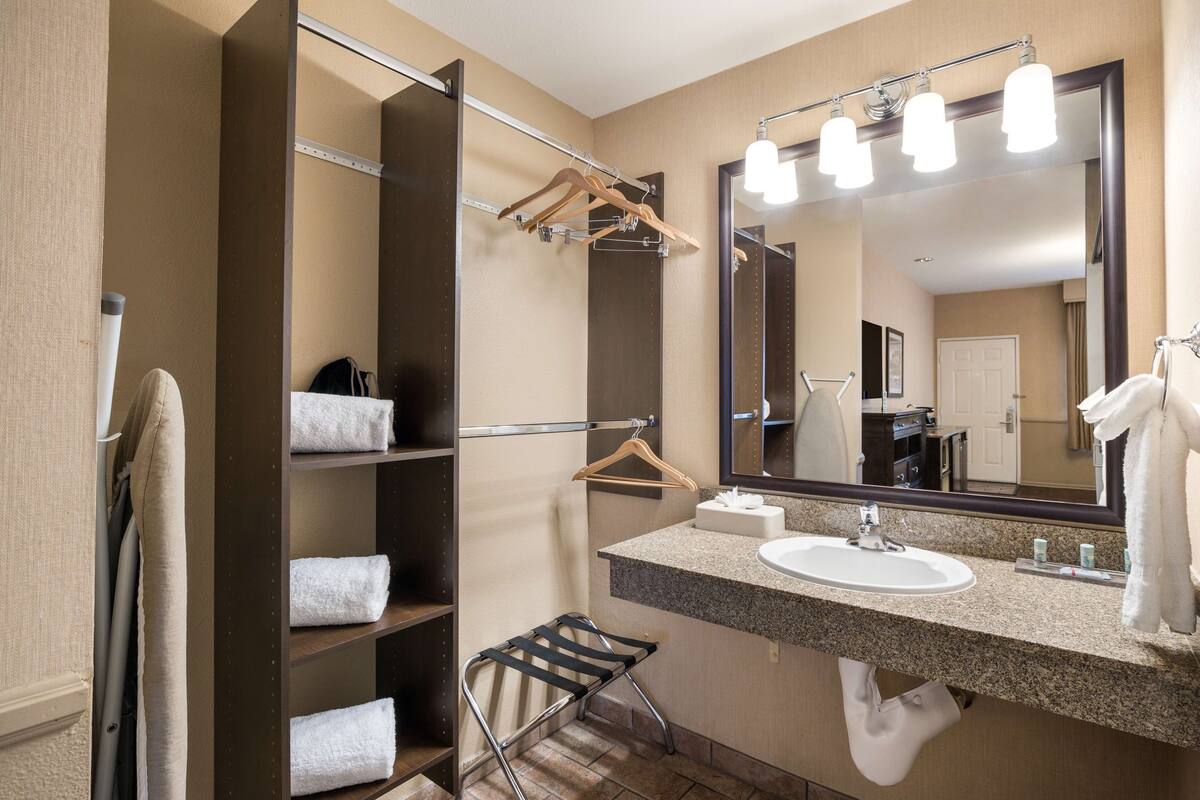 Un baño de hotel con lavamanos, espejo, toallero y repisas con toallas.