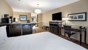 Une chambre d’hôtel avec un grand lit, un bureau avec une chaise, une télévision, une machine à café et un minibar.