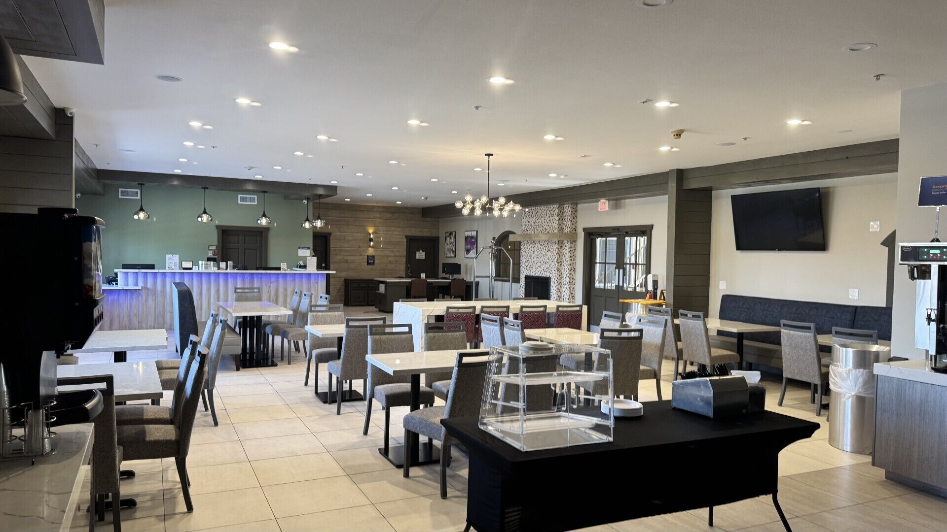 A modern restaurant with multiple dining areas, a bar, and a kitchen visible in the background.