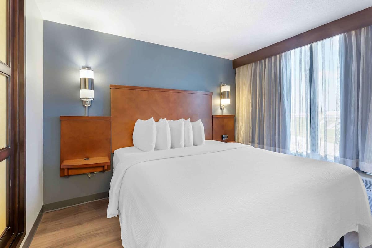 A hotel room with a large bed, wooden headboard, two bedside tables, and a window with sheer curtains.