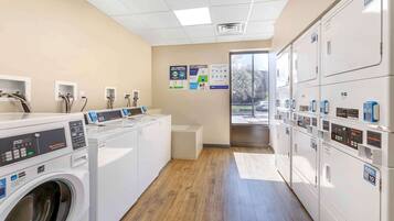 A laundry facility with multiple washing machines and dryers, a control panel, and informational posters on the wall.