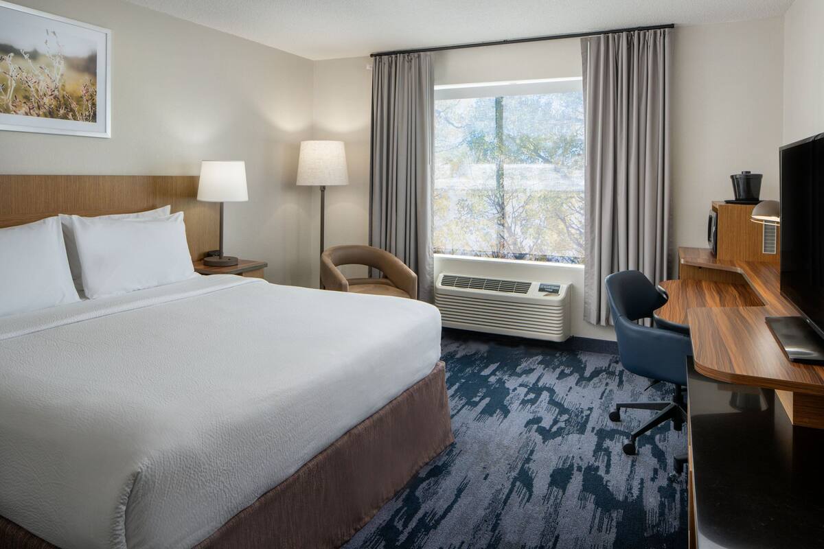 A hotel room with a large bed, a desk with a chair, a television, and a window with curtains.