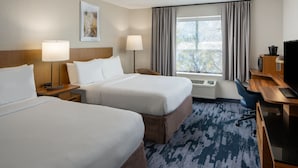 Habitación de hotel con dos camas, un escritorio, una silla, un televisor y una ventana con cortinas.