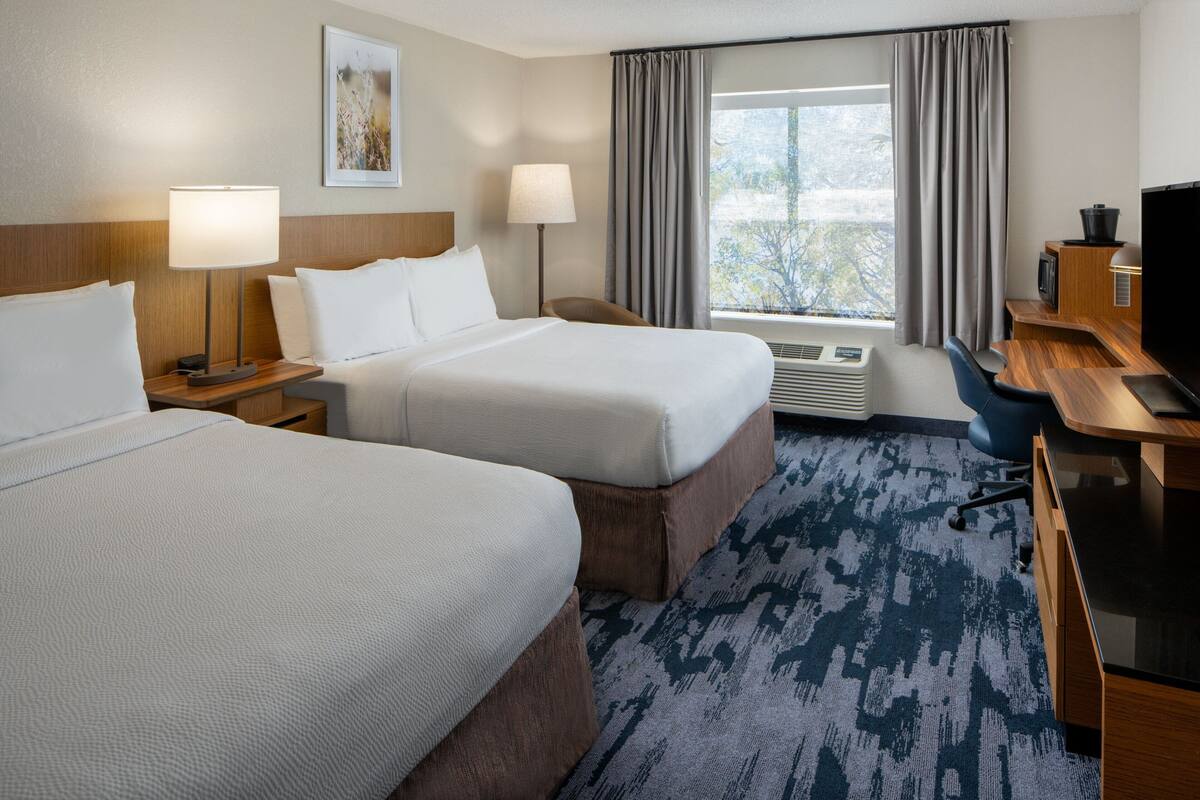 A hotel room with two beds, a desk, a chair, a TV, and a window with curtains.