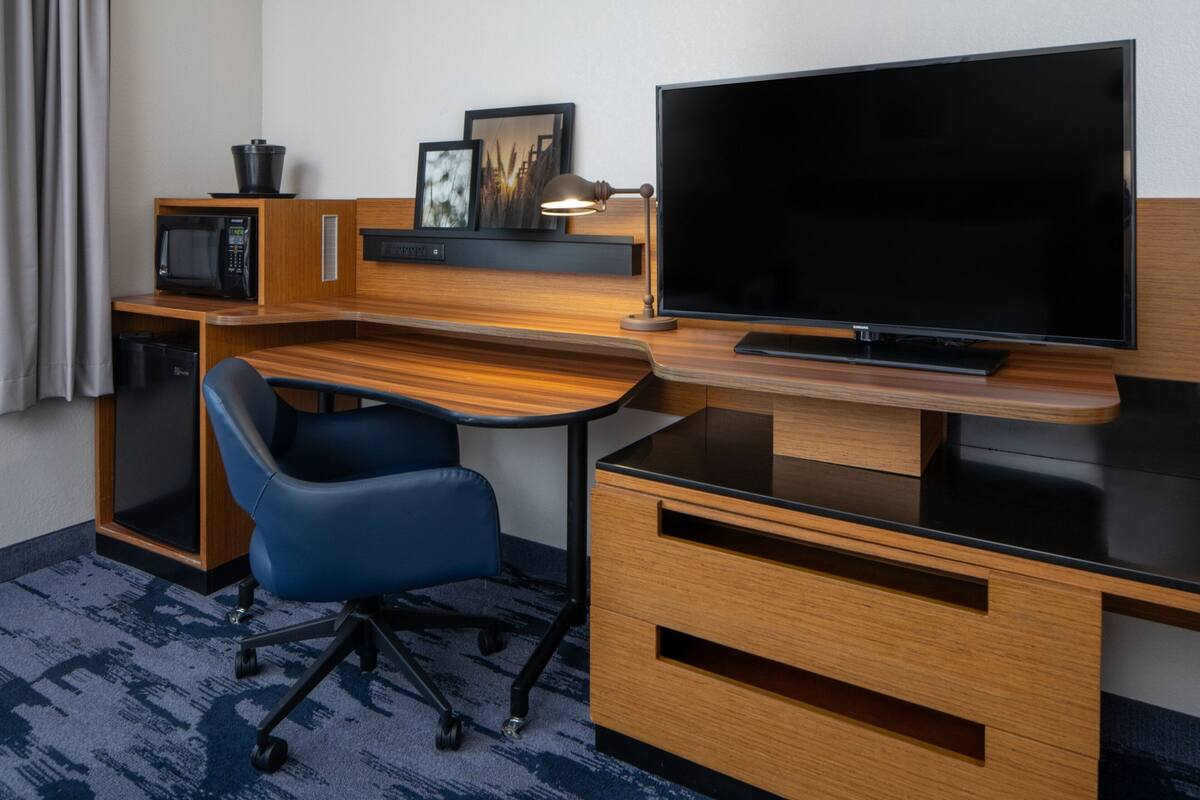 A hotel room with a wooden desk, a television, a microwave, a chair, and a small cabinet.
