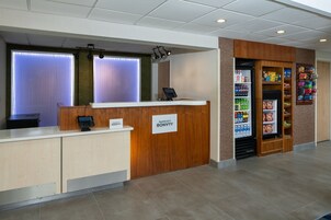 A hotel reception area with a wooden reception desk, a digital phone, and a self-service beverage dispenser.