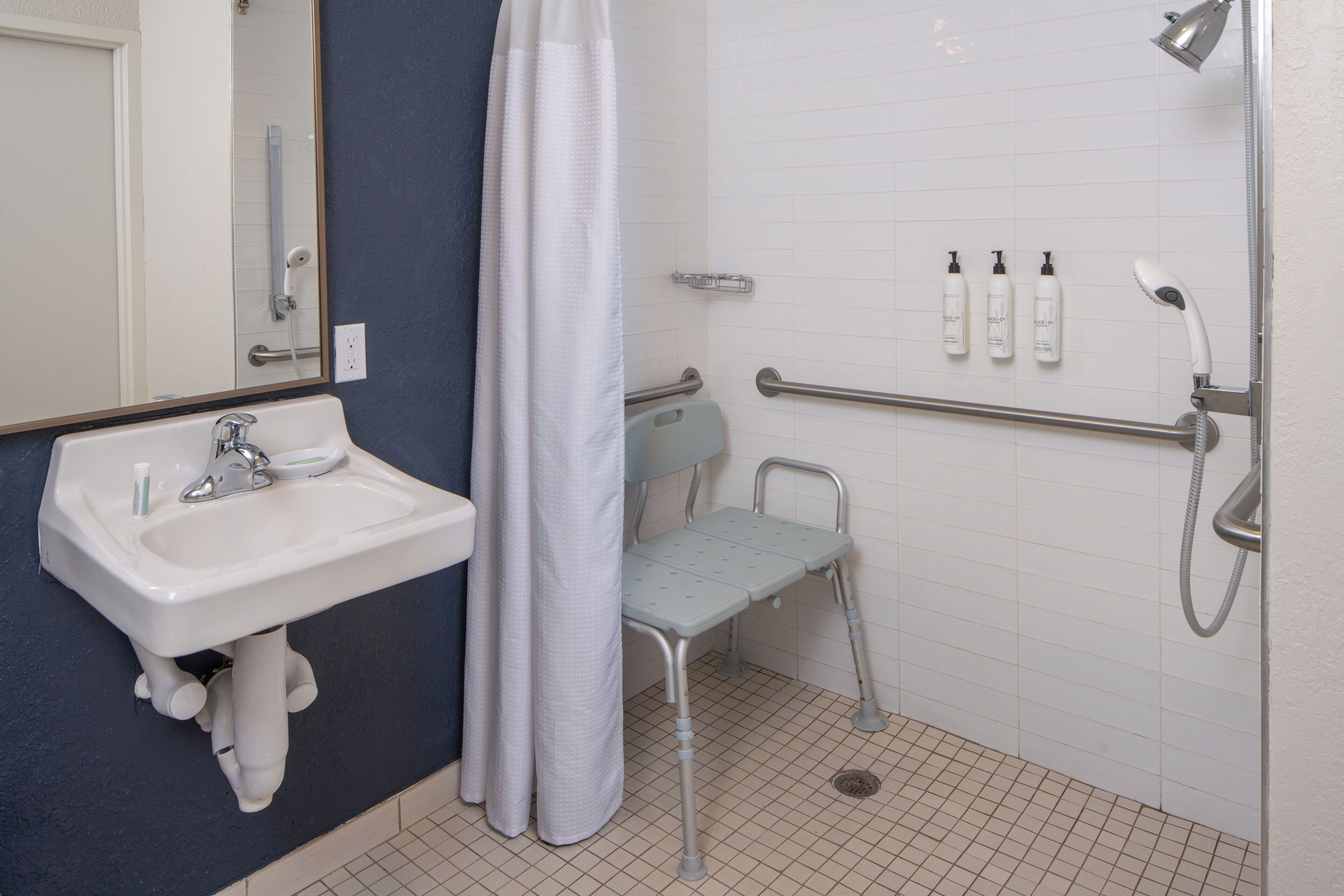 Une salle de bain équipée d’un lavabo, d’une douche, d’un banc accessible aux personnes en fauteuil roulant et de barres d’appui.