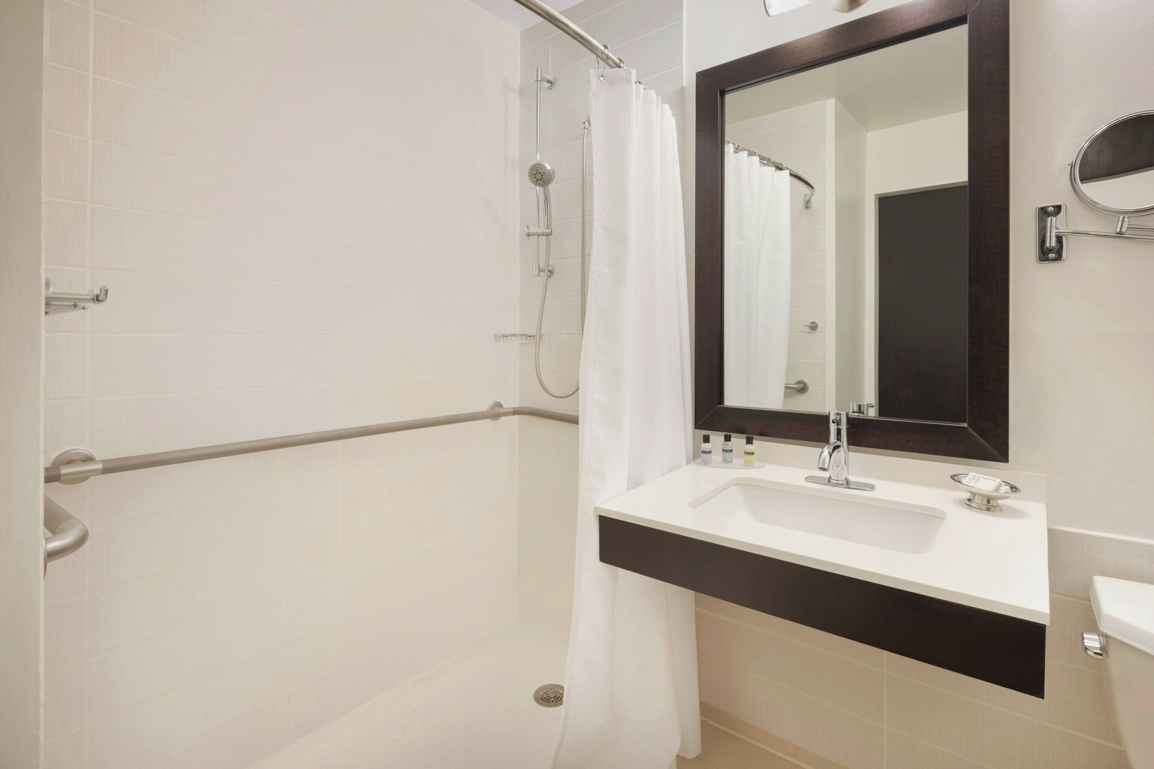 Un baño con ducha, lavamanos y espejo.