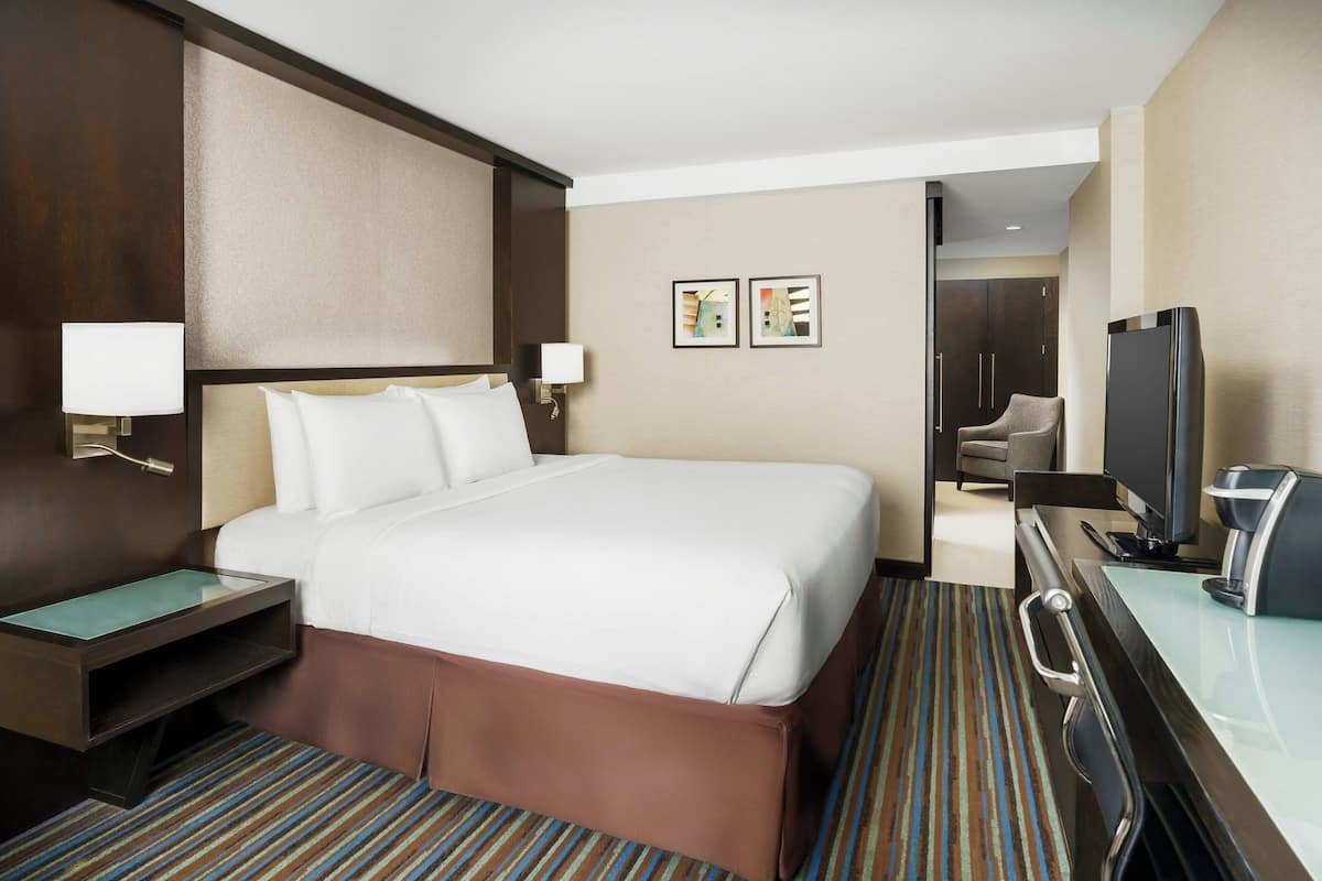 Habitación de hotel con una cama grande, un escritorio con computadora, televisor y cafetera.
