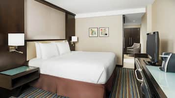 Habitación de hotel con una cama grande, un escritorio con computadora, televisor y cafetera.
