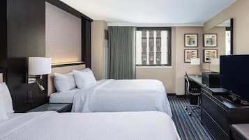 A hotel room with two beds, a desk with a computer, a TV, and a large window with curtains.