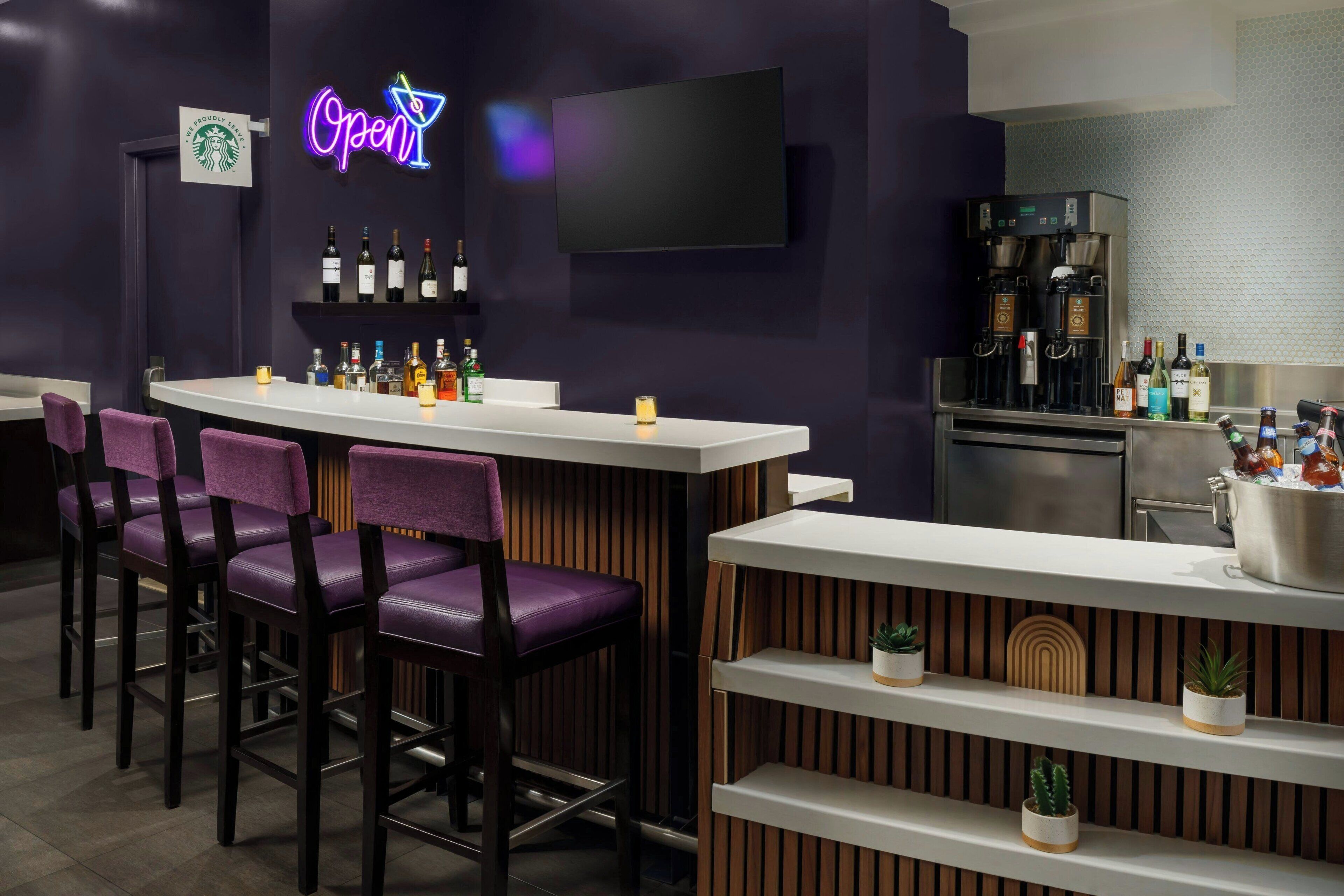 A bar area with purple chairs, a neon 'Open' sign, a TV, and a coffee machine.