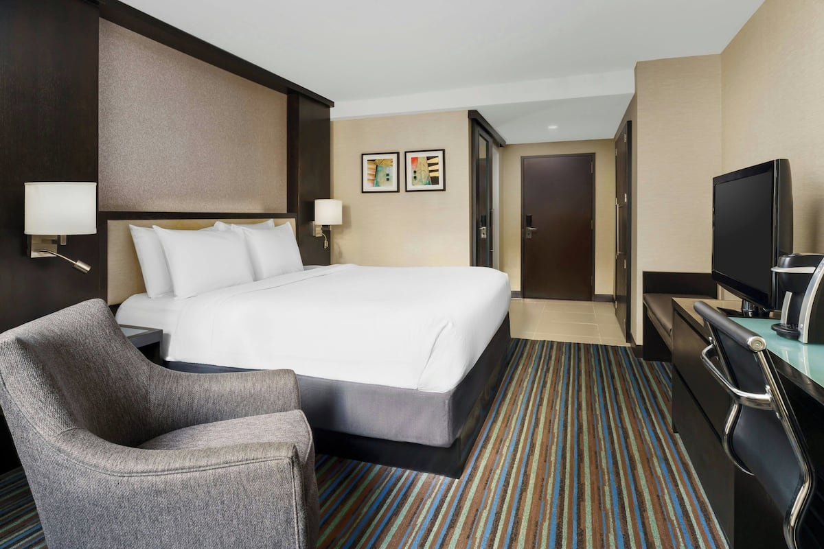 Habitación de hotel con una cama grande, un escritorio con televisor de pantalla plana, una silla y una alfombra a rayas.