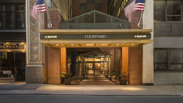 Marriott Courtyard -hotellin sisäänkäynti, jossa on lasinen katos, Yhdysvaltain lippuja ja klassinen arkkitehtoninen tyyli.