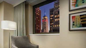 Hotellihuone, josta on näkymä Empire State Building -rakennukseen. Huoneessa on harmaa nojatuoli, lattiavalaisin ja kaksi kehystettyä taideteosta seinällä.