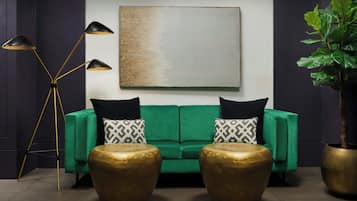 Un salon moderne avec un canapé vert, deux coussins décoratifs à motifs, une lampe sur pied et deux petites tables d’appoint dorées.