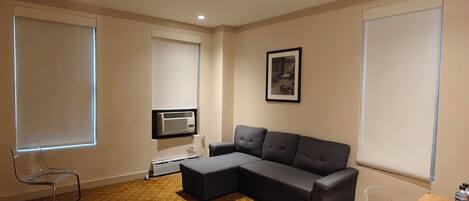 Uma sala de estar moderna com um sofá seccional, uma poltrona transparente e um ar-condicionado fixado na parede.