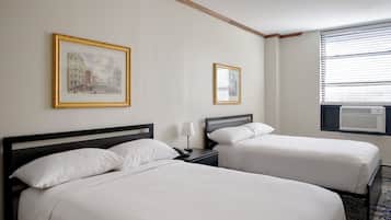 A hotel room with two beds, a nightstand with a lamp, a framed picture on the wall, and an air conditioning unit.