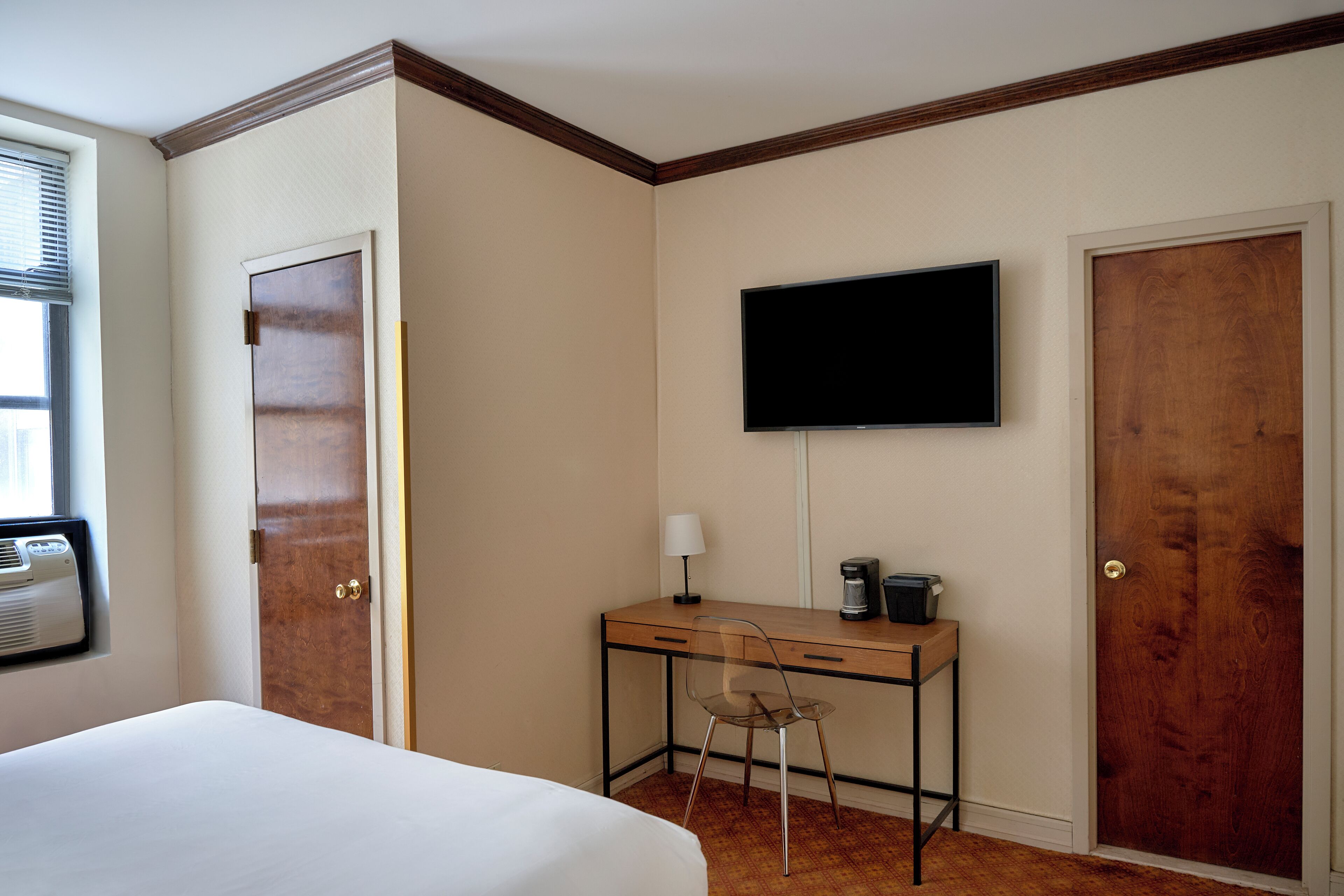 A hotel room with a bed, a desk with a chair, a television, and a window with blinds.