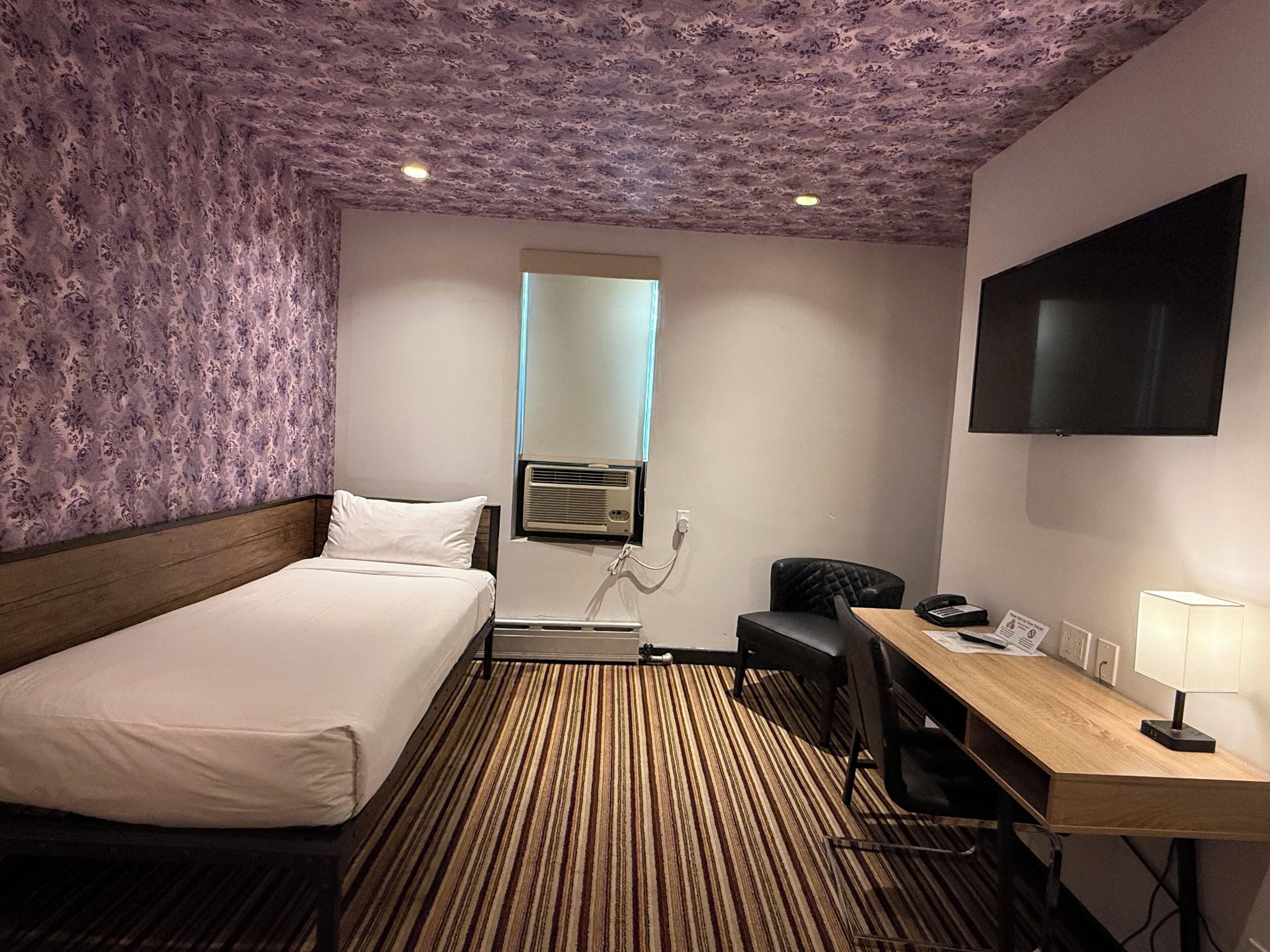 A hotel room with a bed, a desk, a chair, a TV, and a mirror.
