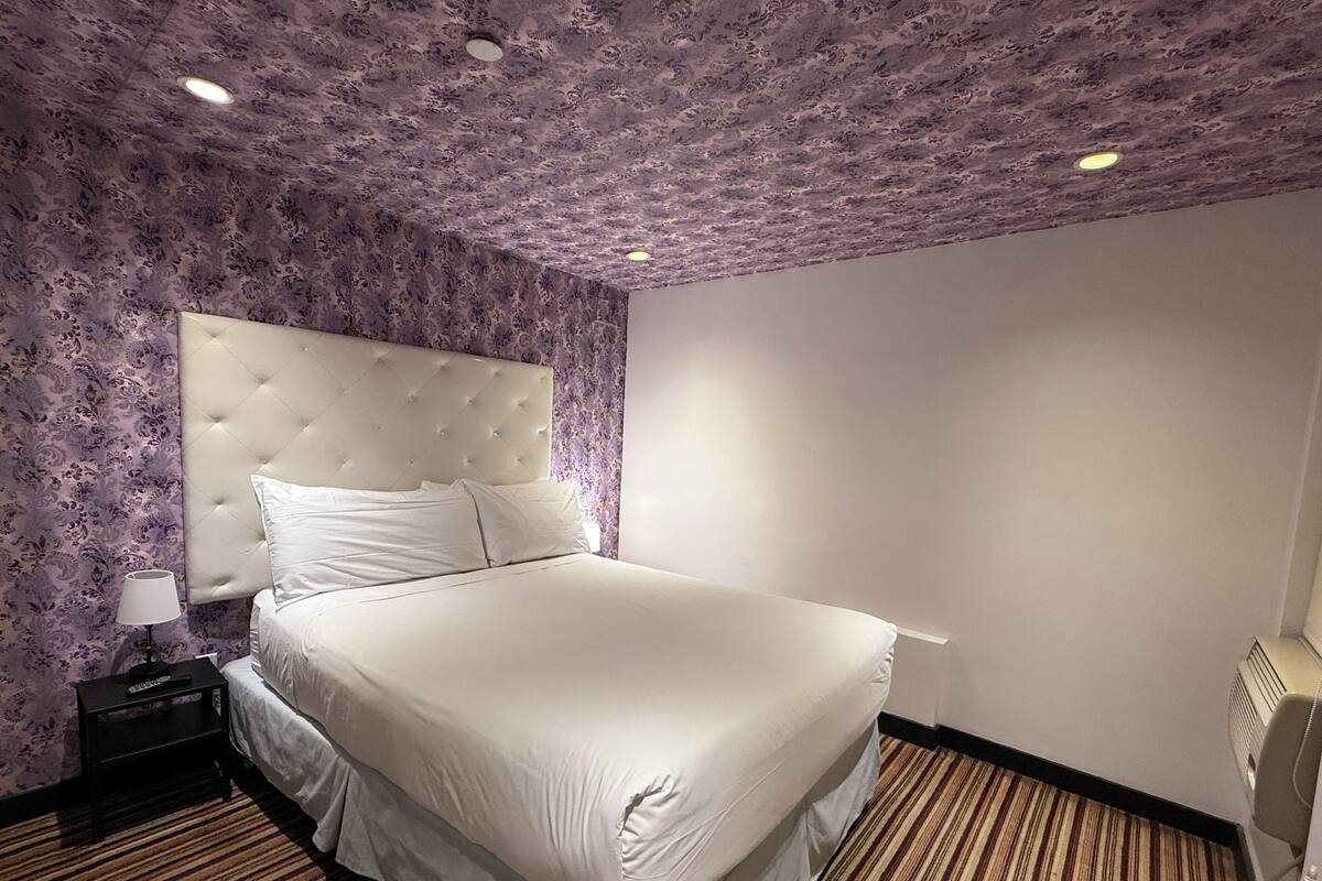 Hotellihuone, jossa on suuri sänky, yöpöytä, lamppu ja kattotuuletin.