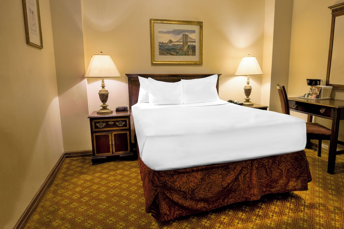A hotel room with a large bed, two bedside lamps, a nightstand, a chair, and a framed picture on the wall.