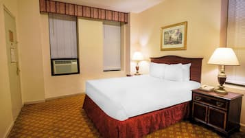 A hotel room with a large bed, two bedside lamps, a nightstand, a telephone, and a window with blinds.