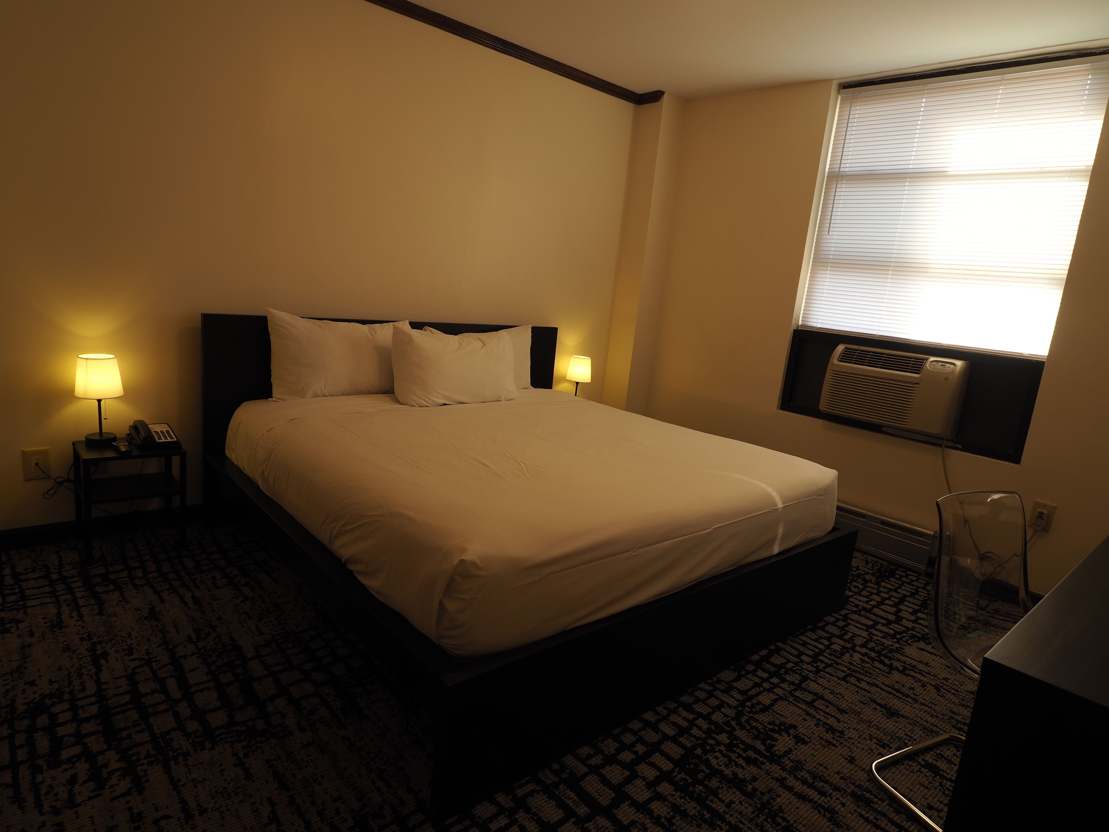 Una habitación de hotel con una cama, dos lámparas de noche, un teléfono y una ventana con persianas.