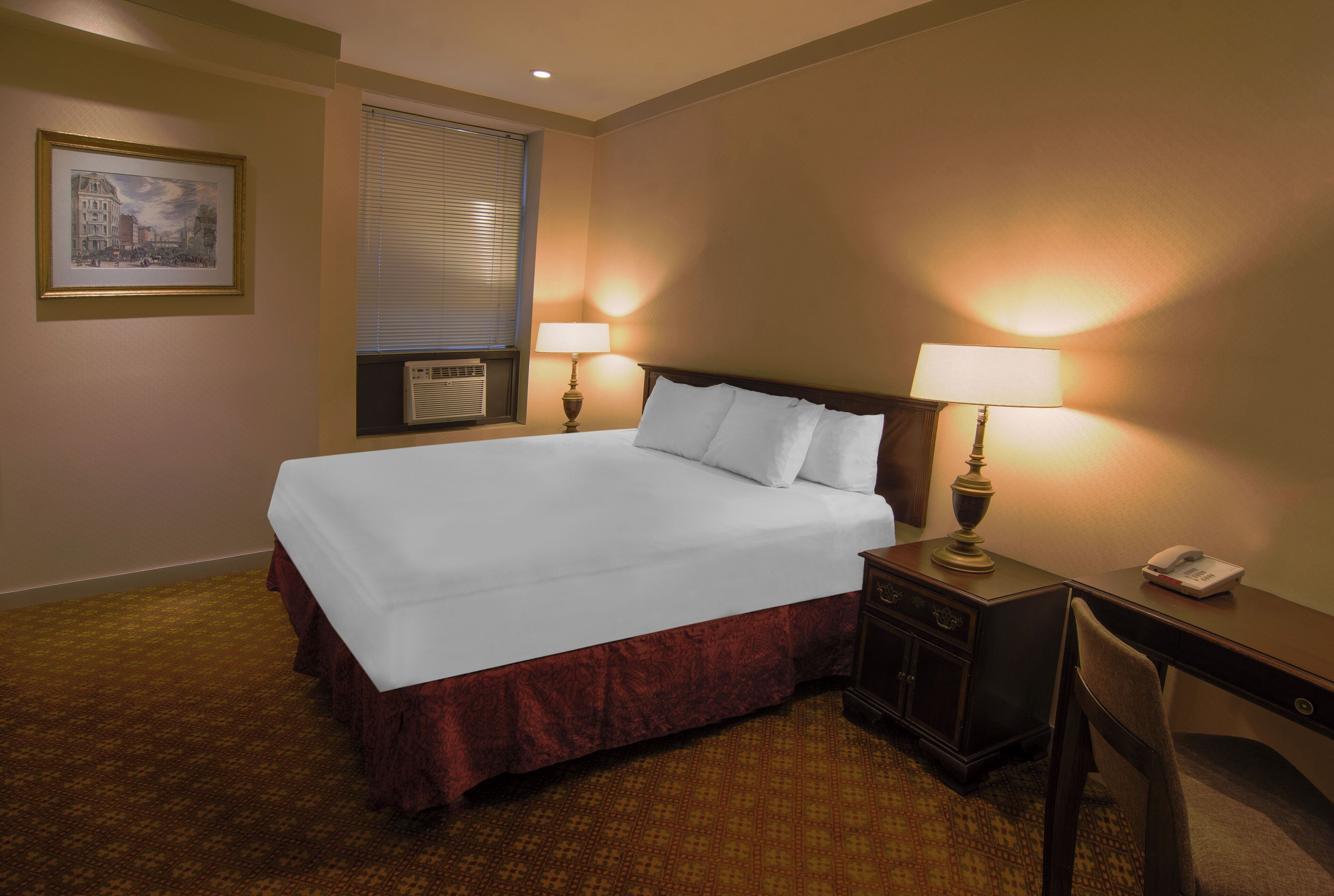 Habitación de hotel con una cama grande, dos lámparas de noche, un escritorio con teléfono y un cuadro en la pared.