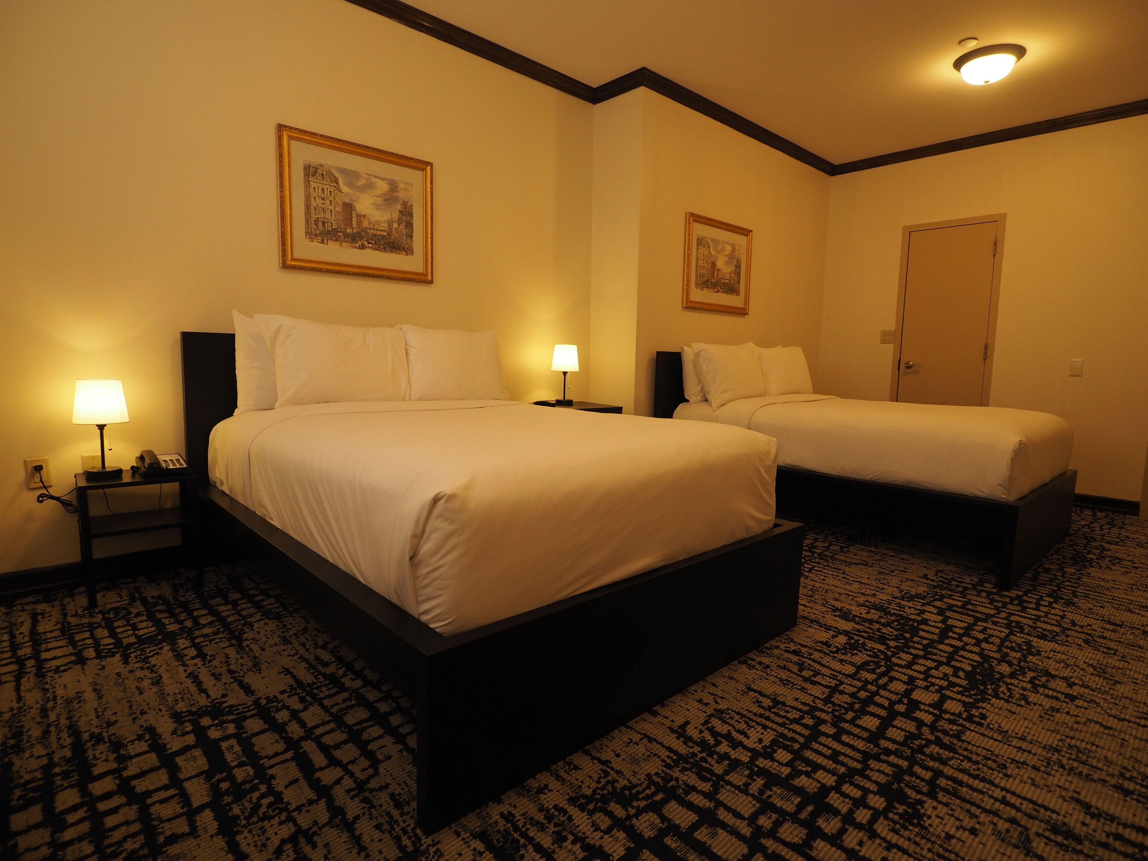 Une chambre d’hôtel avec deux lits, une table de chevet avec une lampe et une porte.