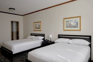 Quarto de hotel com duas camas, mesa de cabeceira com abajur e quadros nas paredes.