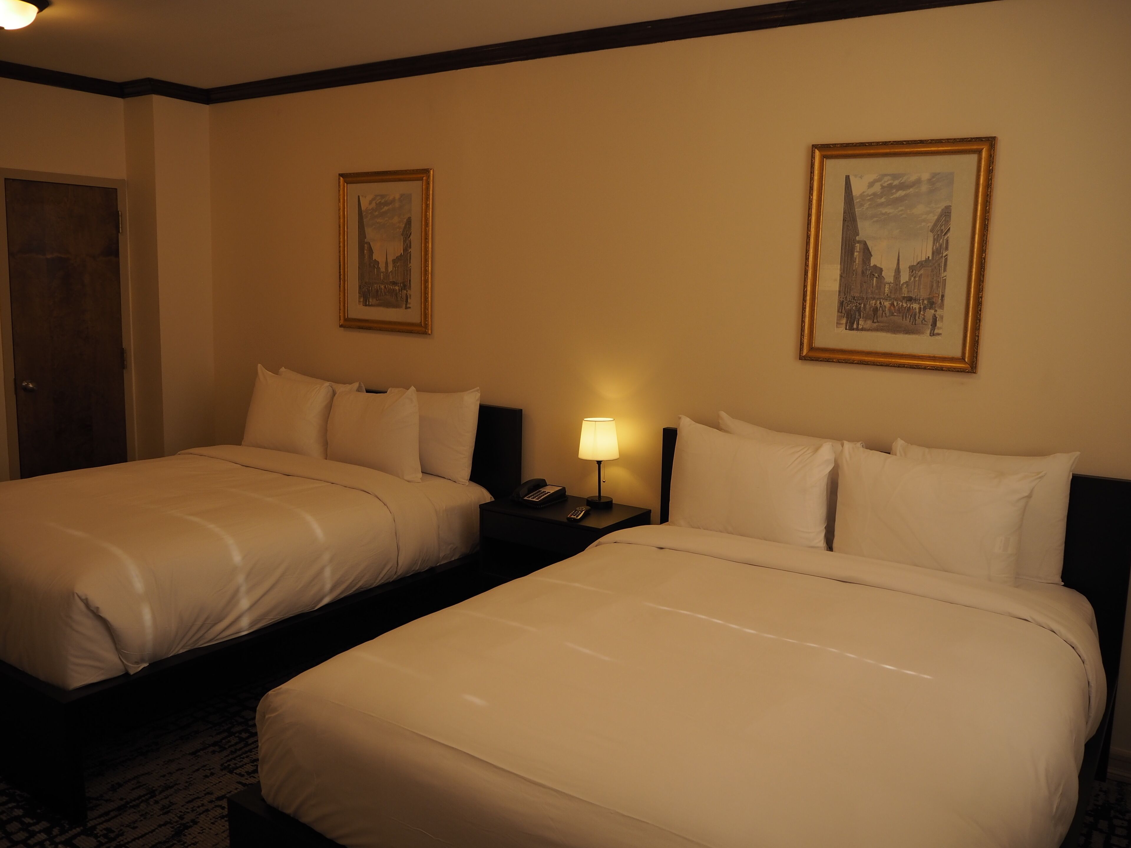 A hotel room with two beds, a nightstand with a lamp, and two framed pictures on the wall.