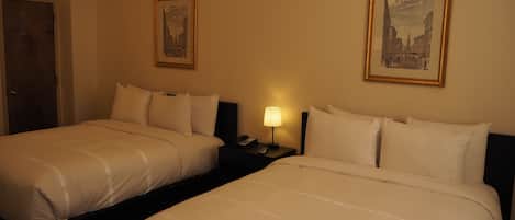 A hotel room with two beds, a nightstand with a lamp, and two framed pictures on the wall.
