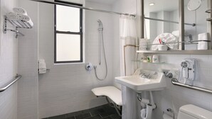 A modern bathroom with a shower, toilet, sink, and a glass shelf with toiletries. - Night Hotel Broadway (New York)