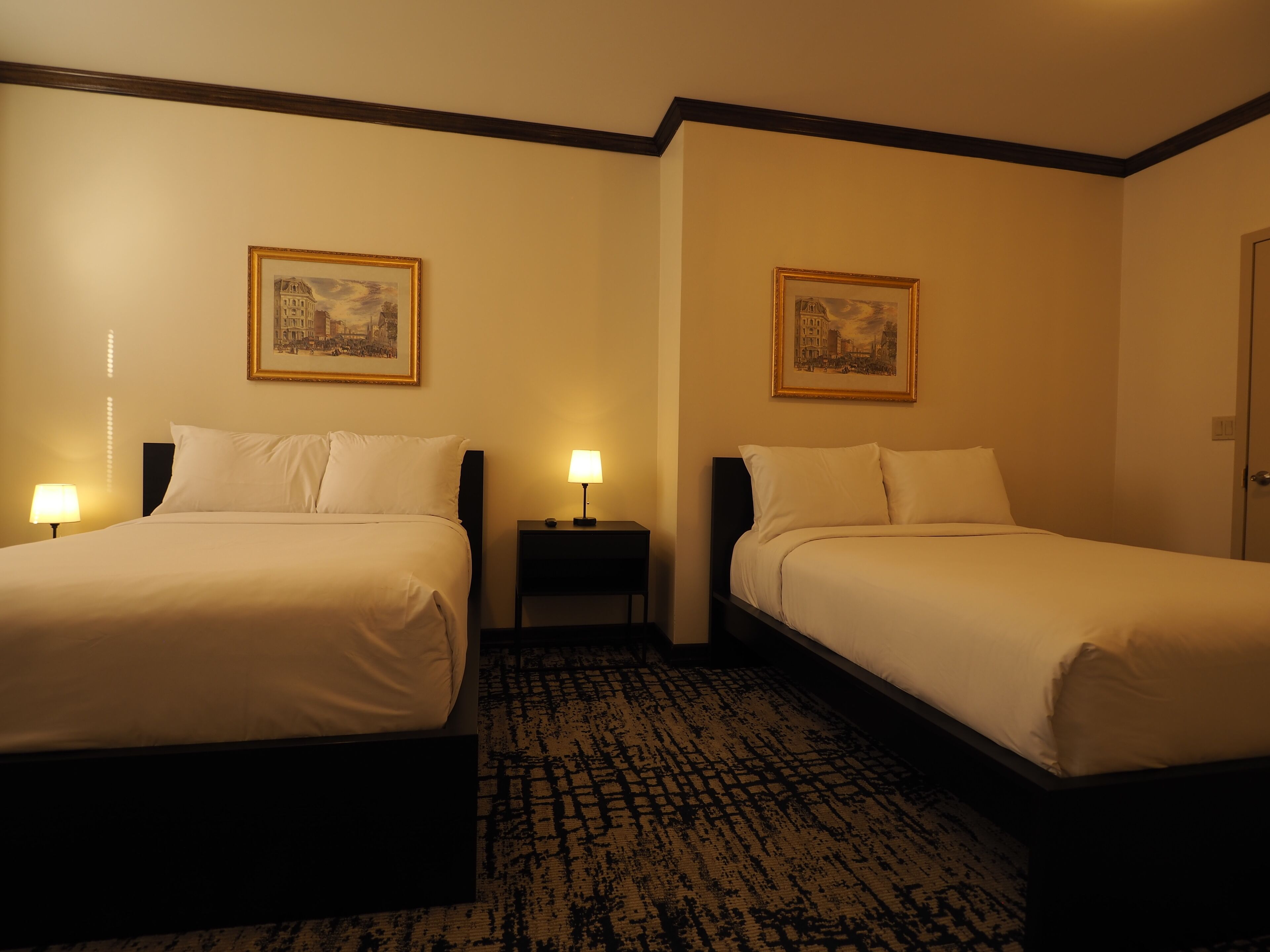 Ein Hotelzimmer mit zwei Betten, einem Nachttisch, einer Lampe und zwei gerahmten Bildern an den Wänden.