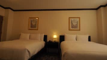 Una habitación de hotel con dos camas, una mesita de noche con lámpara y dos cuadros en la pared.