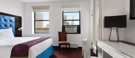 A hotel room with a bed, a desk, a chair, a TV, and windows with city views.