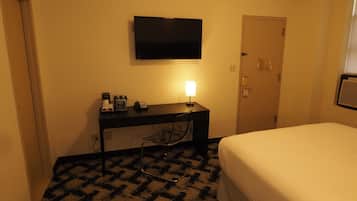 A hotel room with a bed, a desk with a lamp, a flat-screen TV, and a door.