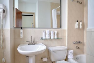 Un baño moderno con lavamanos, inodoro y ducha. Hay toallas y artículos de aseo en estantes.