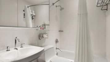Une salle de bain moderne avec un lavabo, des toilettes et une baignoire blancs. On y trouve un rideau de douche, un porte-serviettes et un miroir au-dessus du lavabo.