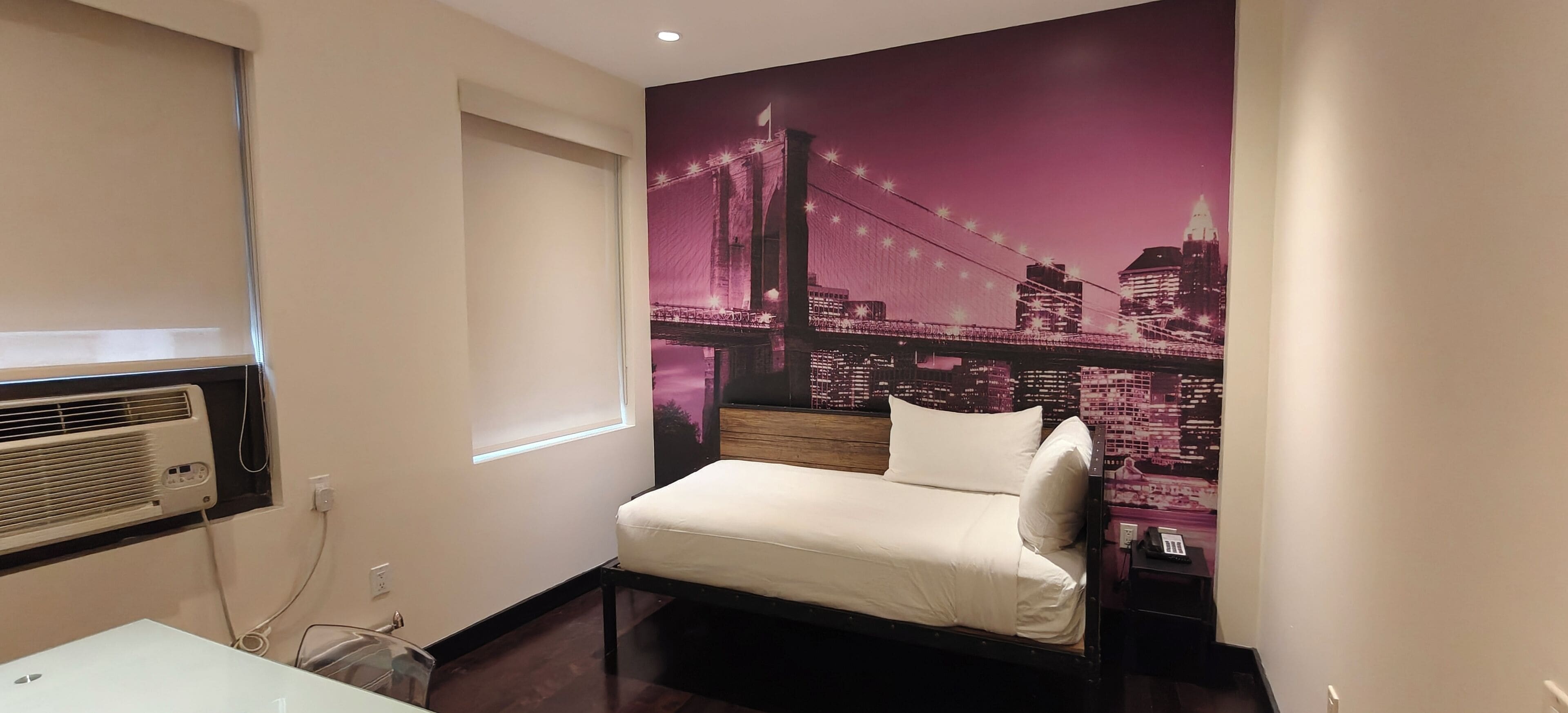 A hotel room with a bed, a window, and a wall mural of a cityscape.