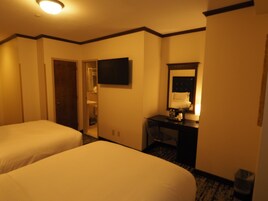 Quarto de hotel com duas camas, uma escrivaninha, um espelho e uma televisão.