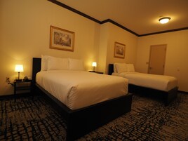 A hotel room with two beds, a nightstand with a lamp, and a door.